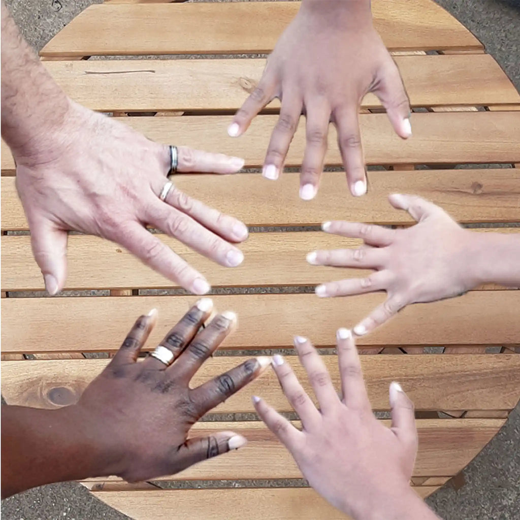A circle of diverse hands joined together over a wooden surface, symbolising the family-owned roots and community of the brand. 