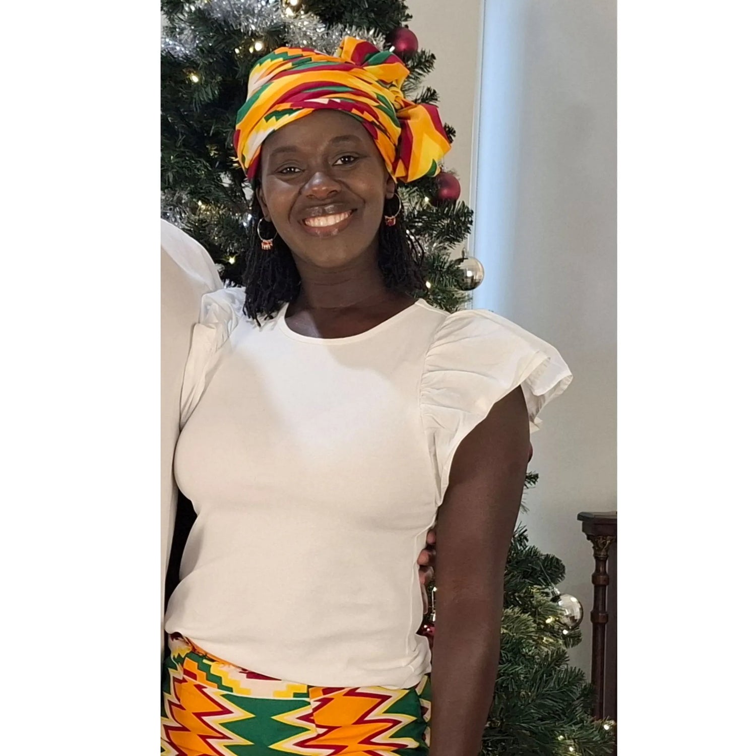 See My Curls founder Ruth Wallis smiling and wearing a colorful traditional headwrap, used to introduce her personal journey and the mission behind her natural hair care brand.