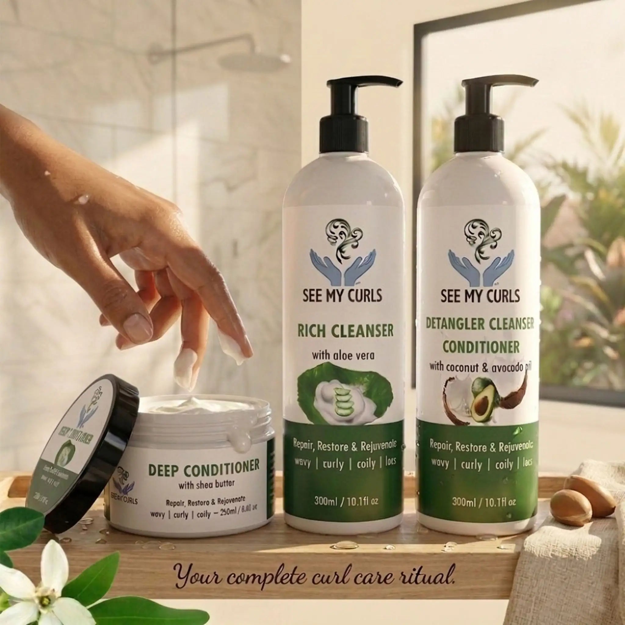 A lifestyle shot of the See My Curls hair care line on a wooden tray in a bright bathroom. From left to right: a 250ml Deep Conditioner jar with its black lid resting nearby, a 300ml Rich Cleanser pump bottle (aloe vera), and a 300ml Detangler Cleanser Conditioner pump bottle (coconut & avocado). A hand is shown dipping fingers into the thick white deep conditioner.