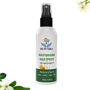 A 125ml (4.2 fl oz) spray bottle of "See My Curls Moisturising Hair Spritz with sweet orange oil." The bottle features a clean white label with a teal blue logo showing hands holding a curly hair illustration, green and blue text, and a dark teal bottom section that reads "Moisturise & Nourish | wavy | curly | coily | locs." The product is centered against a white background with subtle green leaves and white flowers in the bottom left corner.